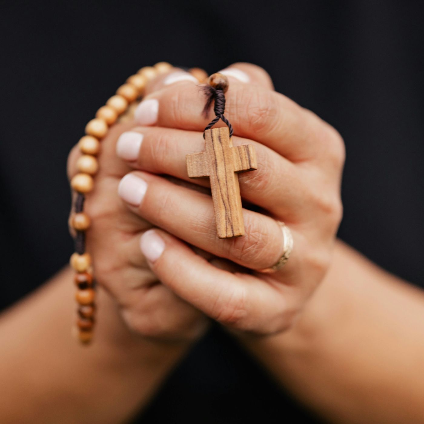 A person holding a wooden rosary with a wooden cross pendant, symbolizing devotion and prayer. Visit www.blessedcatholic.com for handcrafted rosaries and other sacred devotional accessories.